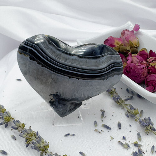 Heart shaped black stripe agate stone displayed on a clear stand with dried flowers around
