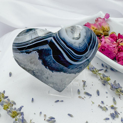 Heart shaped black stripe agate stone displayed with dried flowers on a white cloth