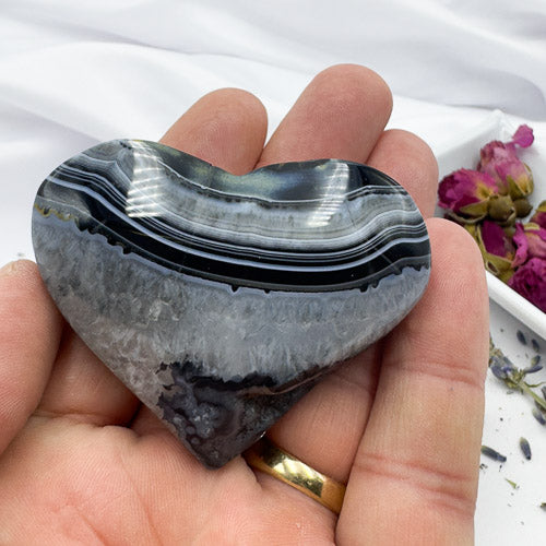 Heart shaped black stripe agate stone held in hand with natural banded patterns and polished surface