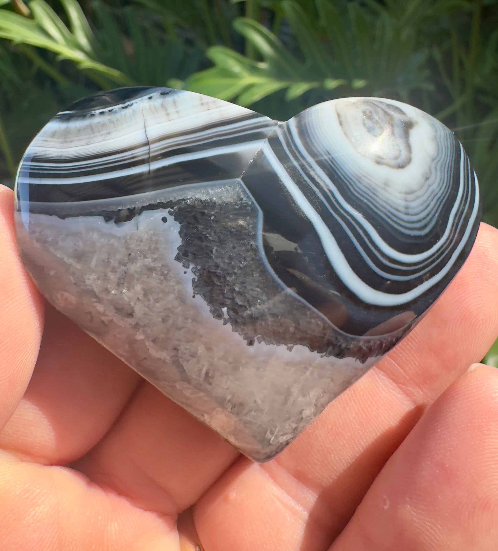 Hand holding a polished heart shaped black stripe agate stone with natural banded patterns