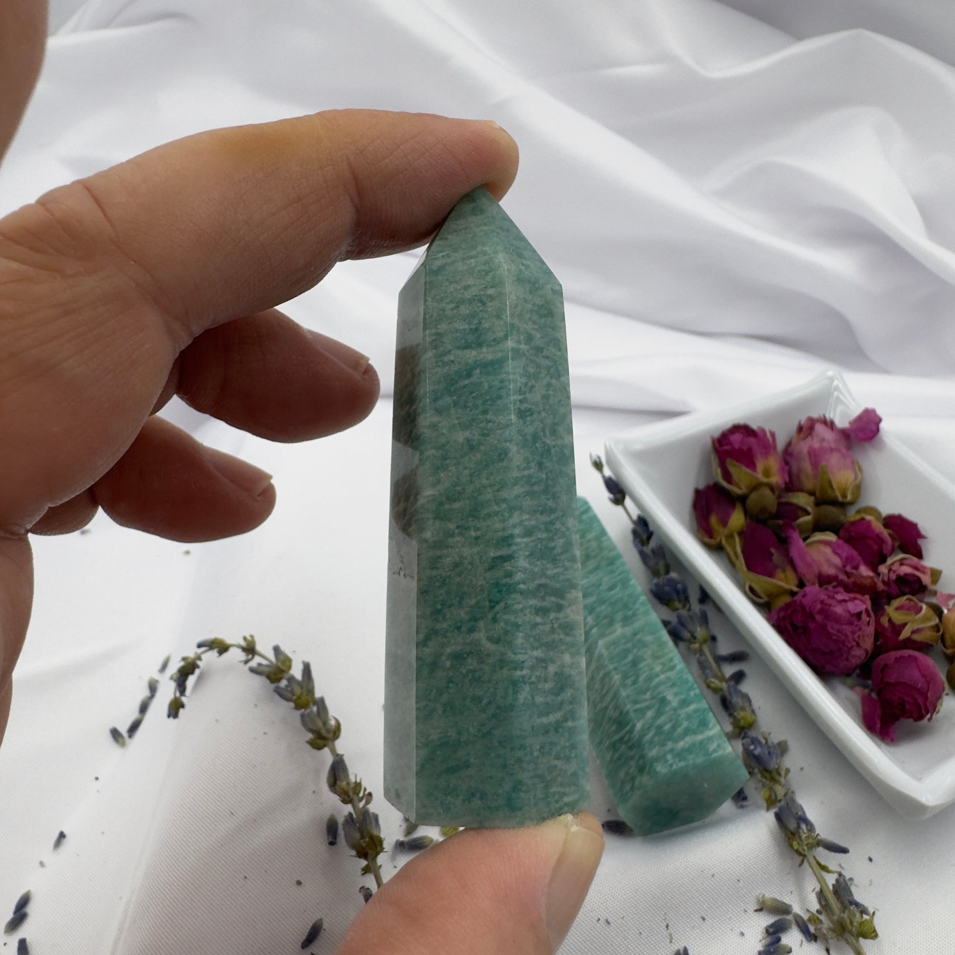 Hand holding polished amazonite tower crystal with dried flowers on white fabric background