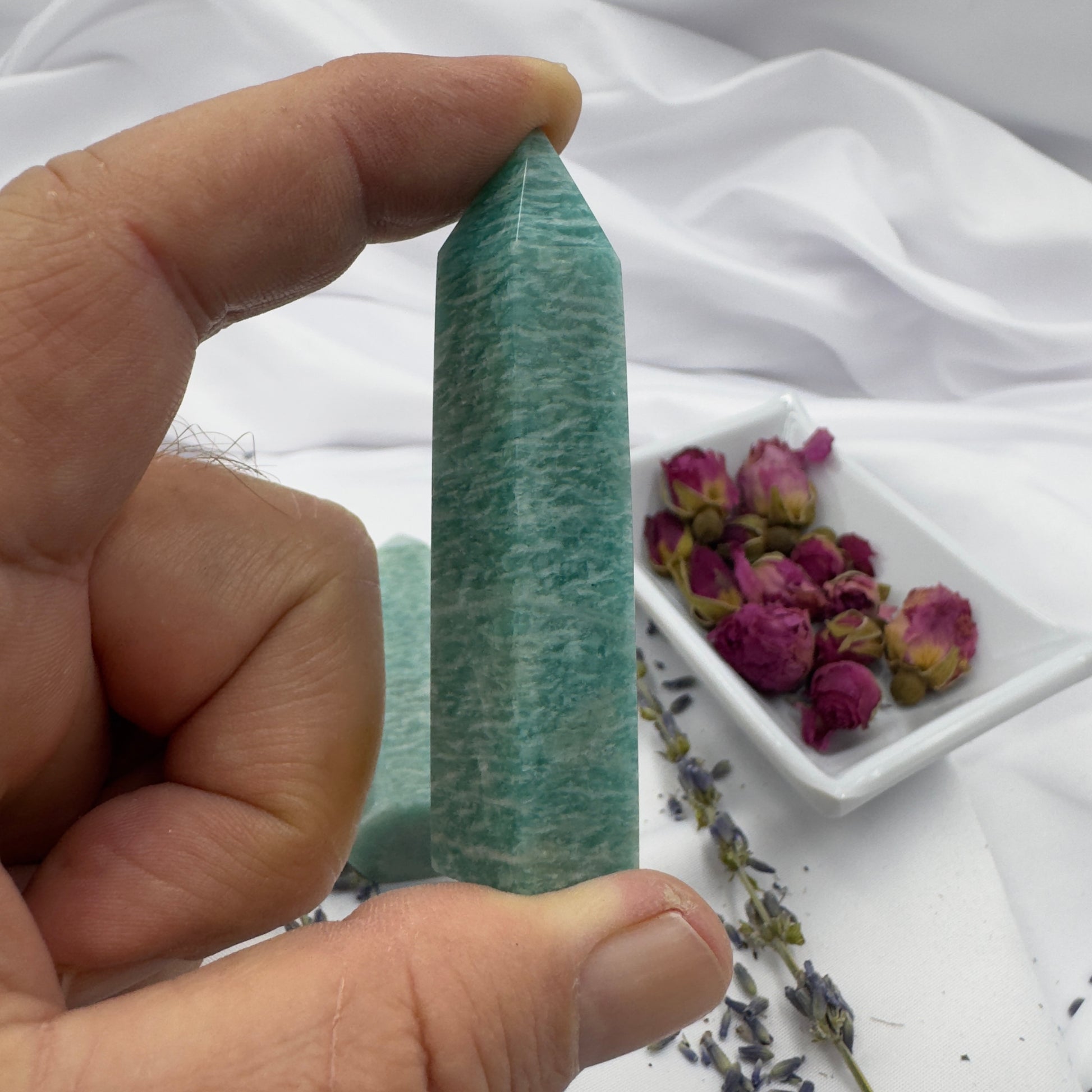Hand holding a polished amazonite tower crystal with dried flowers on a white cloth background