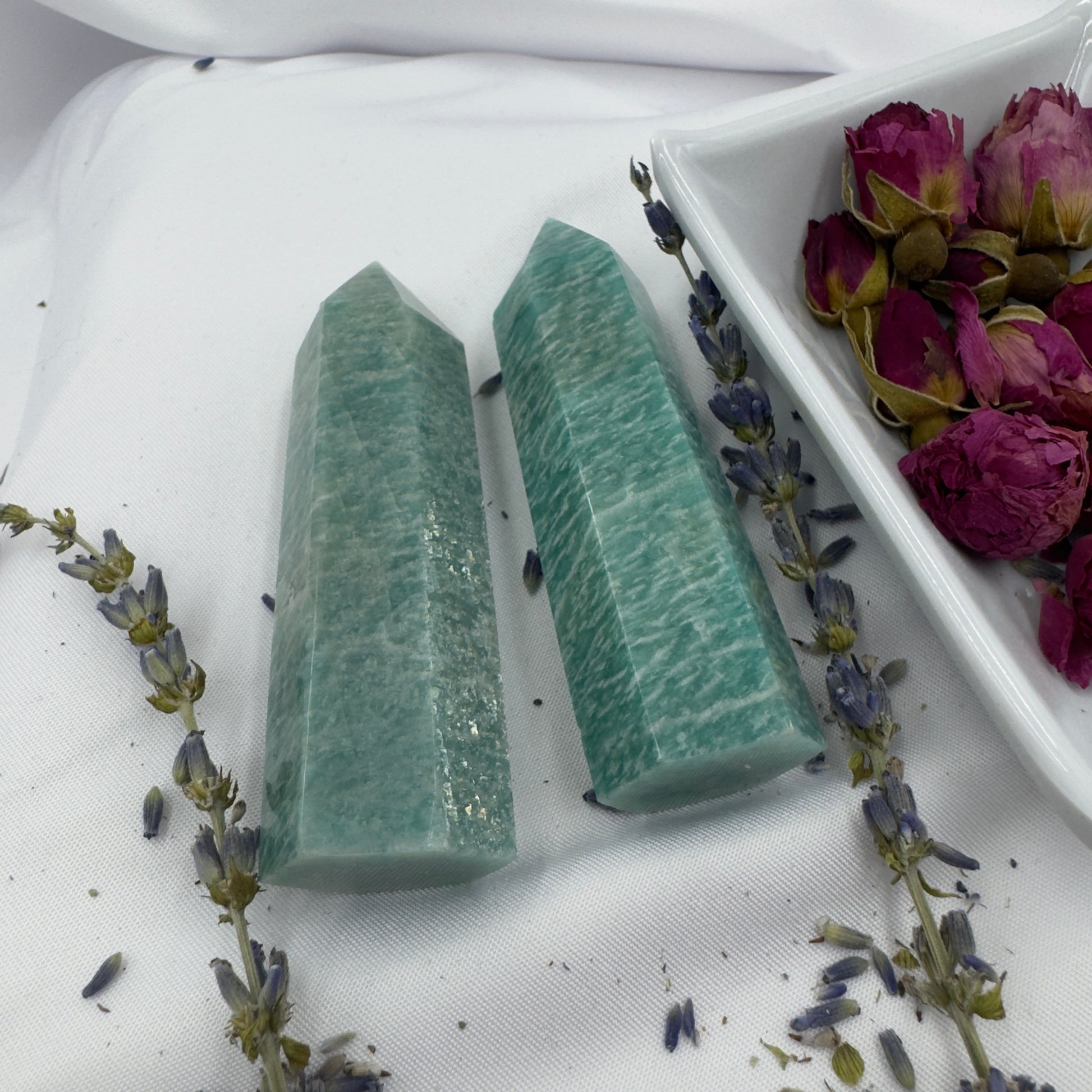 Two polished amazonite tower crystal points on white fabric with dried lavender and rosebuds nearby
