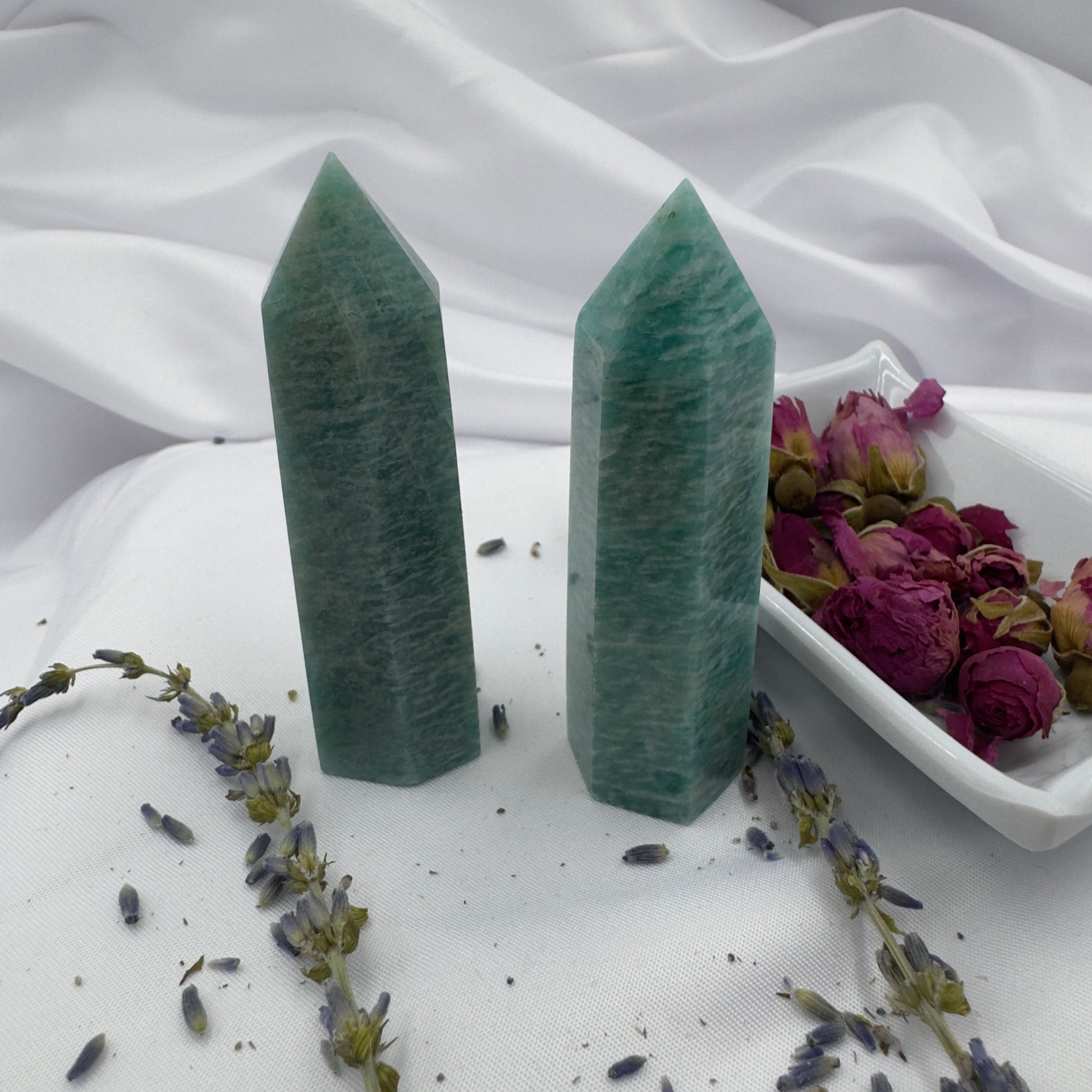 Two polished amazonite tower crystal stones standing on white fabric with dried flowers nearby