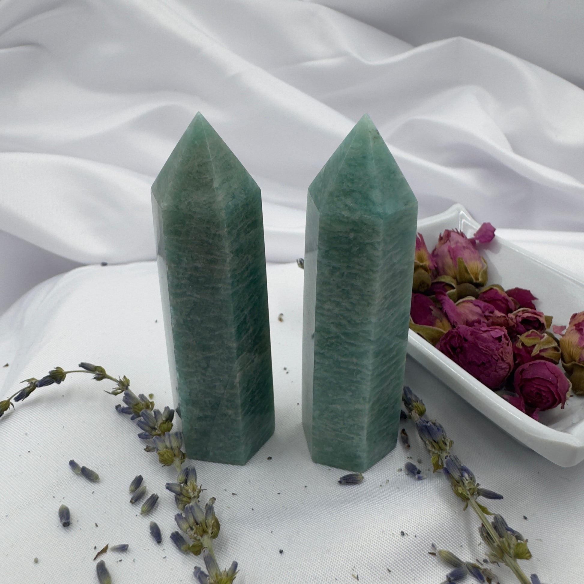 Two green amazonite tower crystal points standing on white fabric surrounded by dried flowers