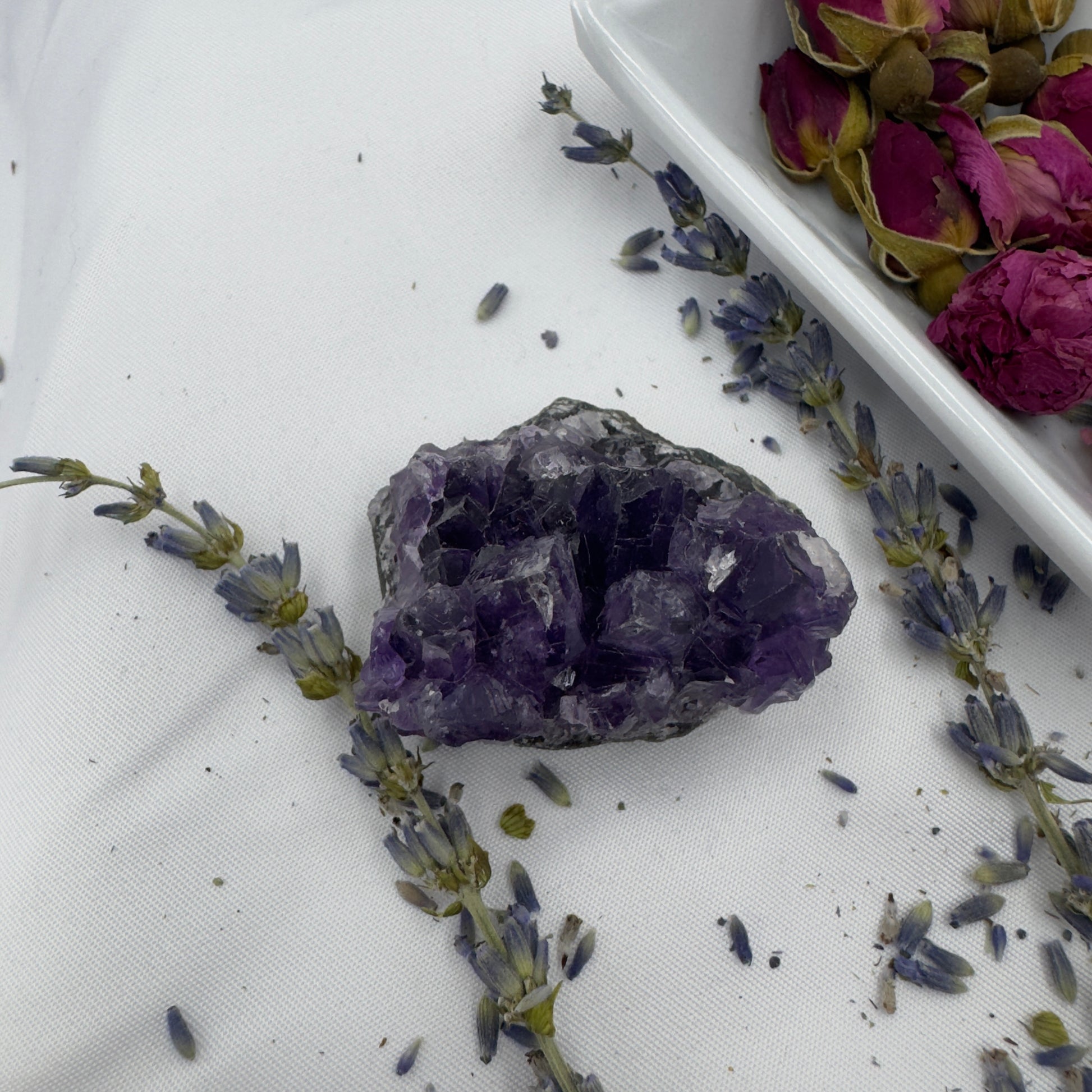 Davinas amethyst raw crystal cluster surrounded by dried lavender and rose petals on white fabric