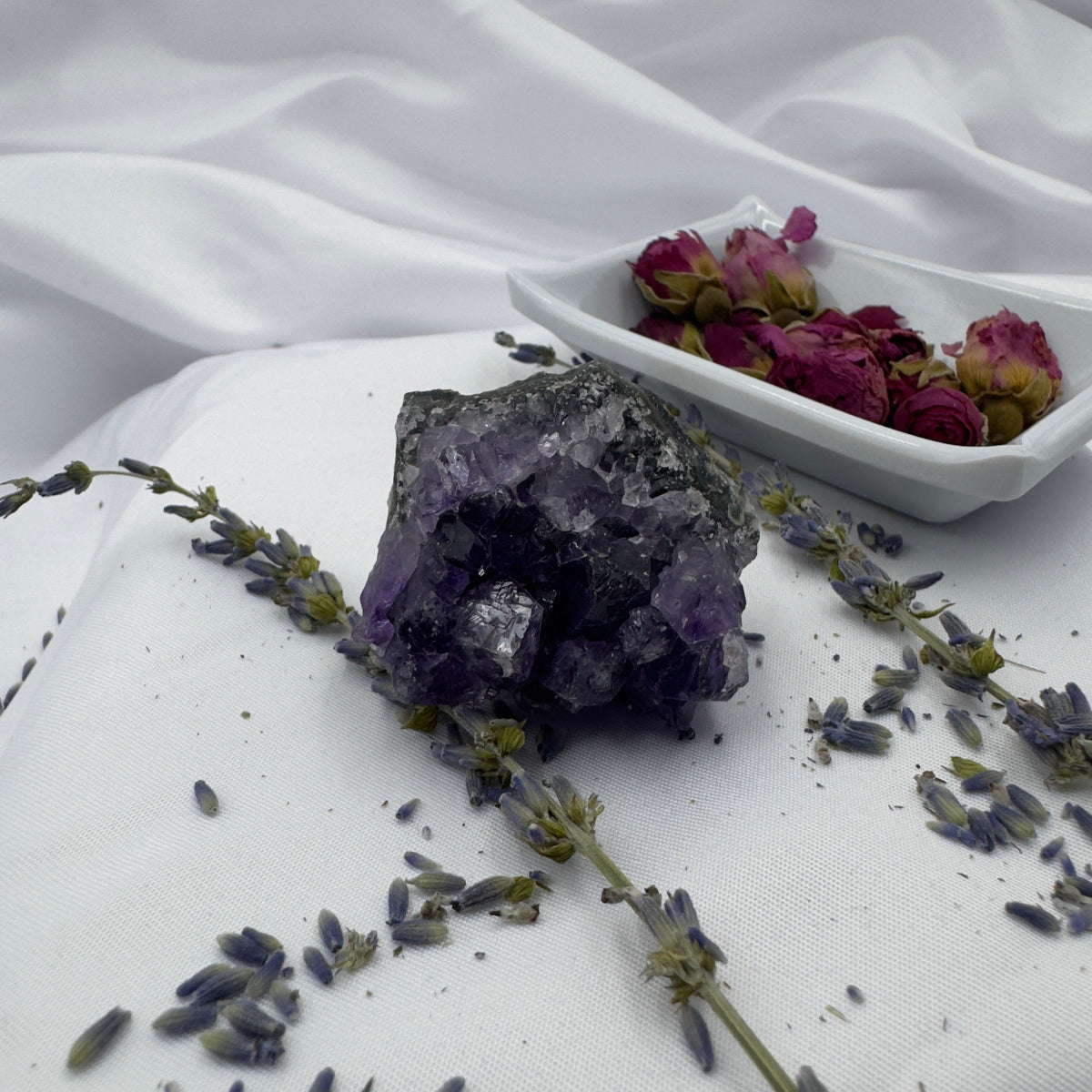 Davinas amethyst raw crystal cluster surrounded by dried lavender and rose buds on white fabric