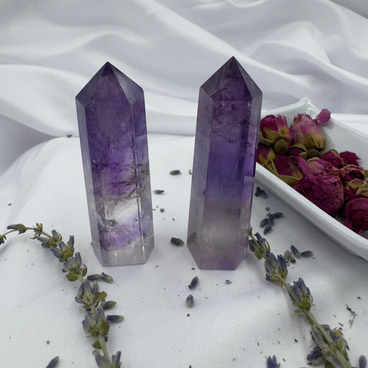 Two polished Amethyst Tower Point crystals standing on white fabric next to dried flowers