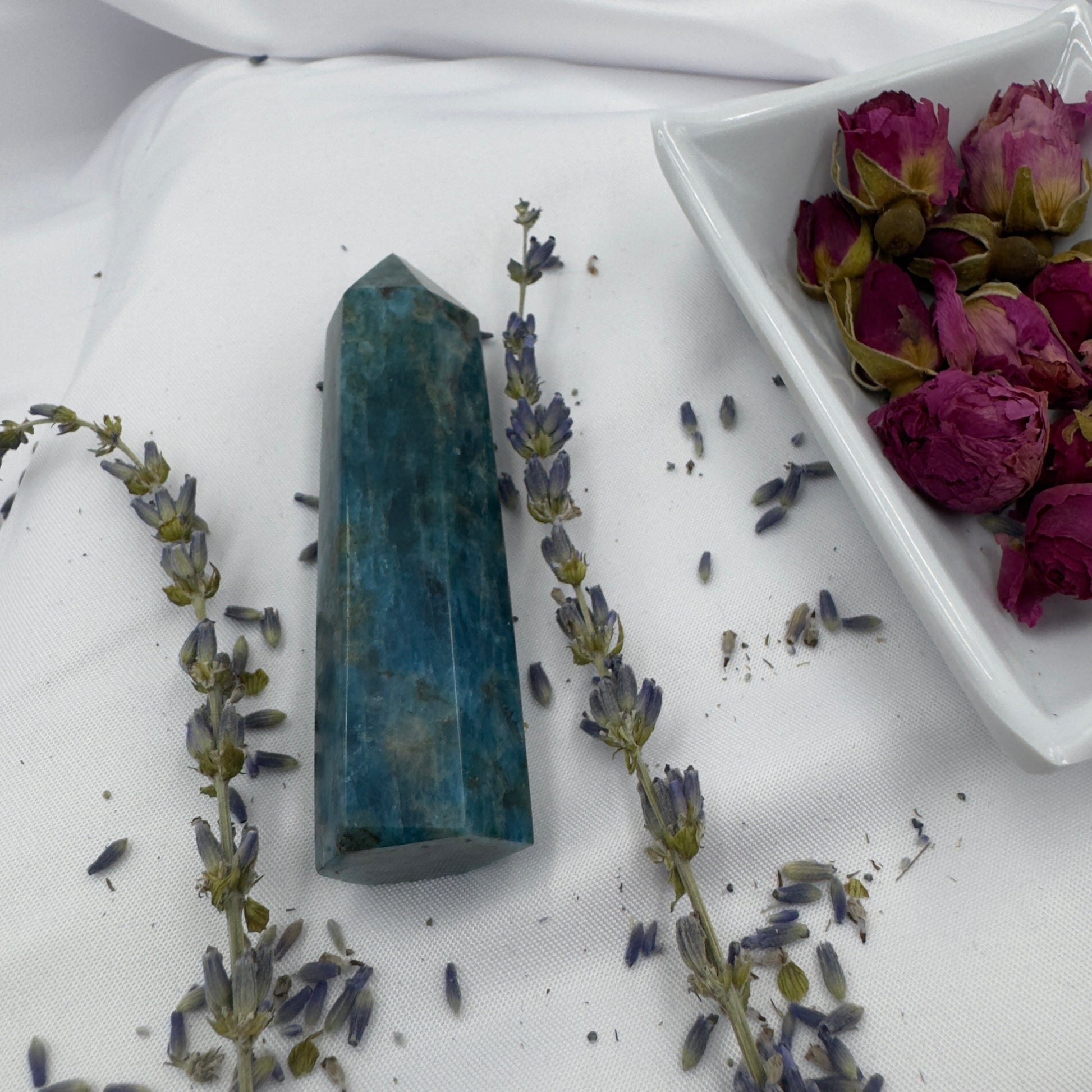 Davinas Apatite Tower Point crystal surrounded by dried lavender and rosebuds on white fabric