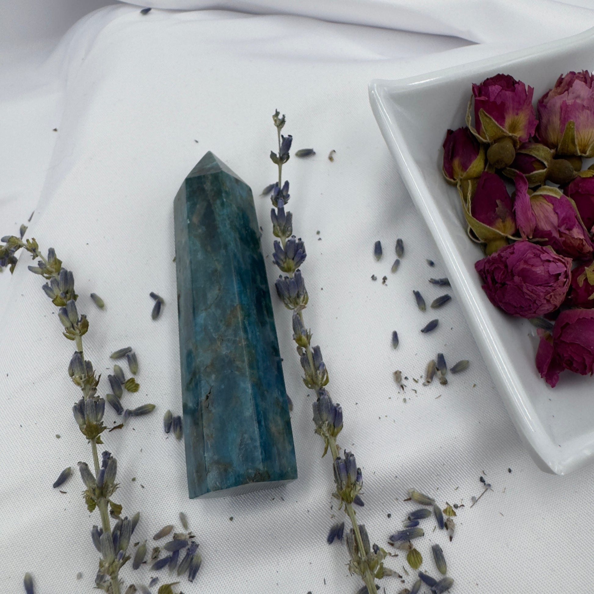 Davinas Apatite Tower Point crystal with blue hues surrounded by dried lavender and rose buds on white fabric