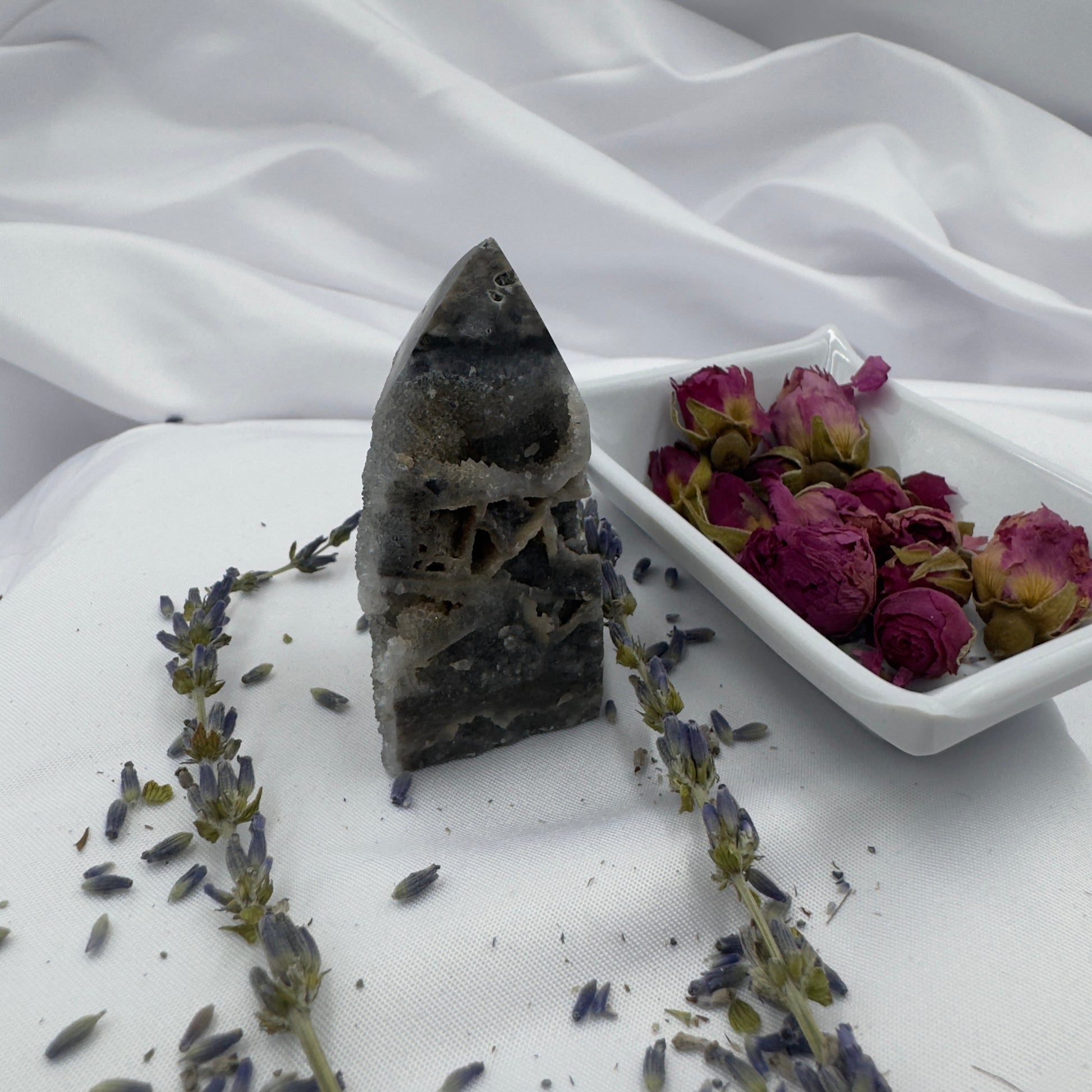 Black Sphalerite Geode Tower with natural crystal formations displayed on white fabric with dried lavender and rose petals