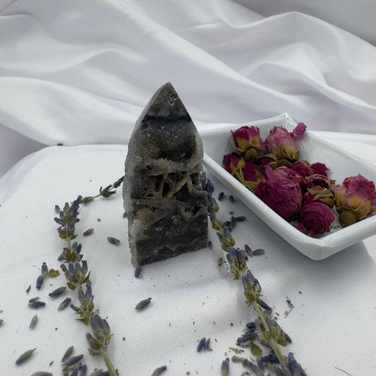 Black Sphalerite Geode Tower with natural crystal formations displayed on white fabric with dried lavender and rose petals