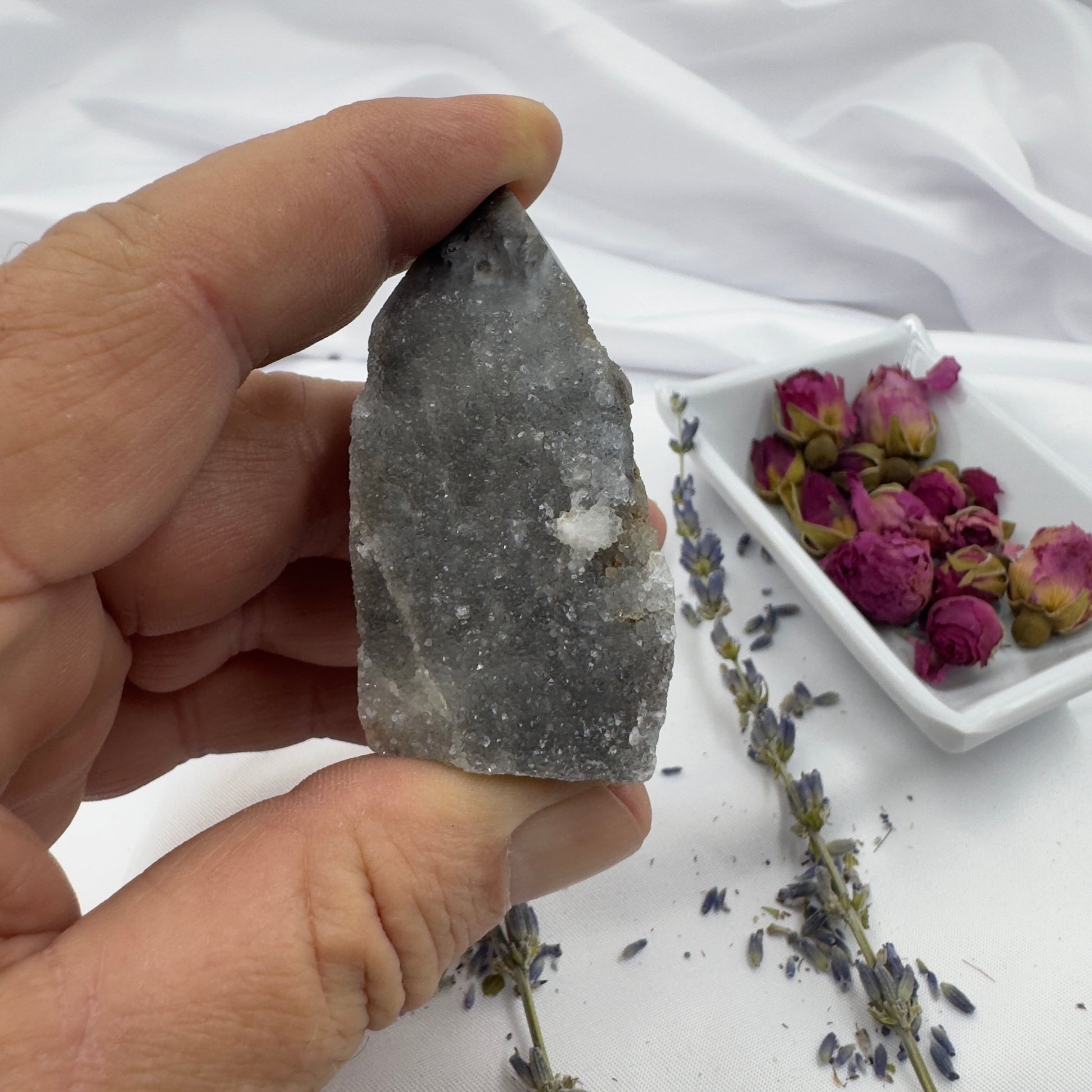 Hand holding a Black Sphalerite Geode Tower with dried flowers and lavender on white background
