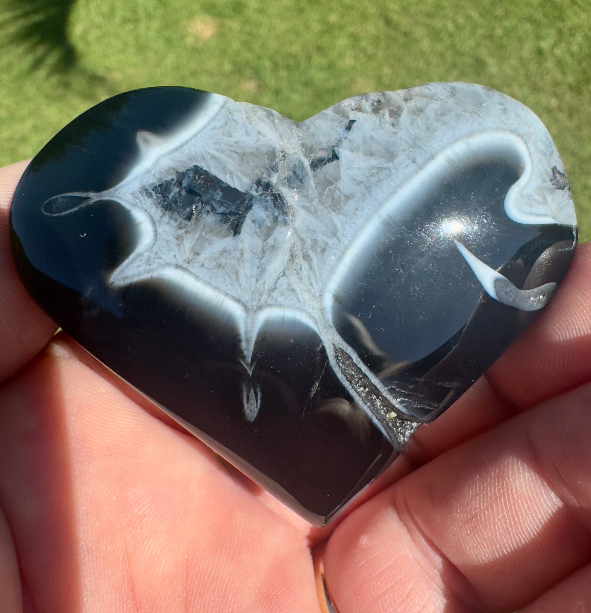 Heart-shaped black stripe agate stone with white and gray patterns held in hand under sunlight