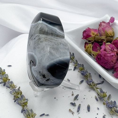 Polished black stripe agate stone displayed on a clear stand with dried flowers around it