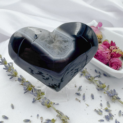 Davinas heart-shaped black stripe agate stone with a polished surface and crystal center on white fabric with dried flowers