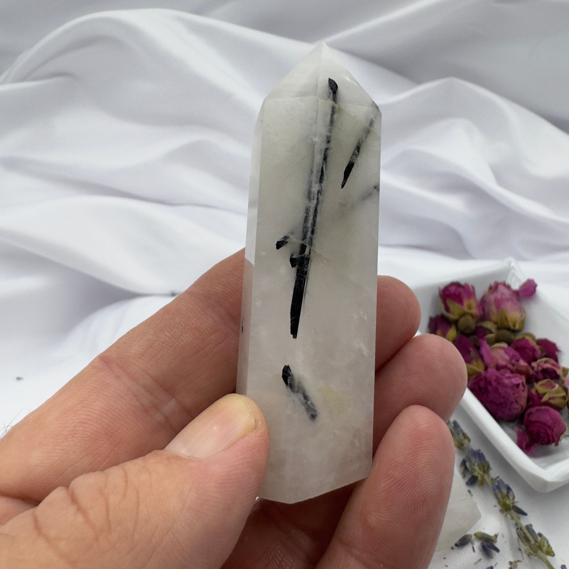 Hand holding a polished black tourmaline tower crystal with white and black streaks against a white fabric background