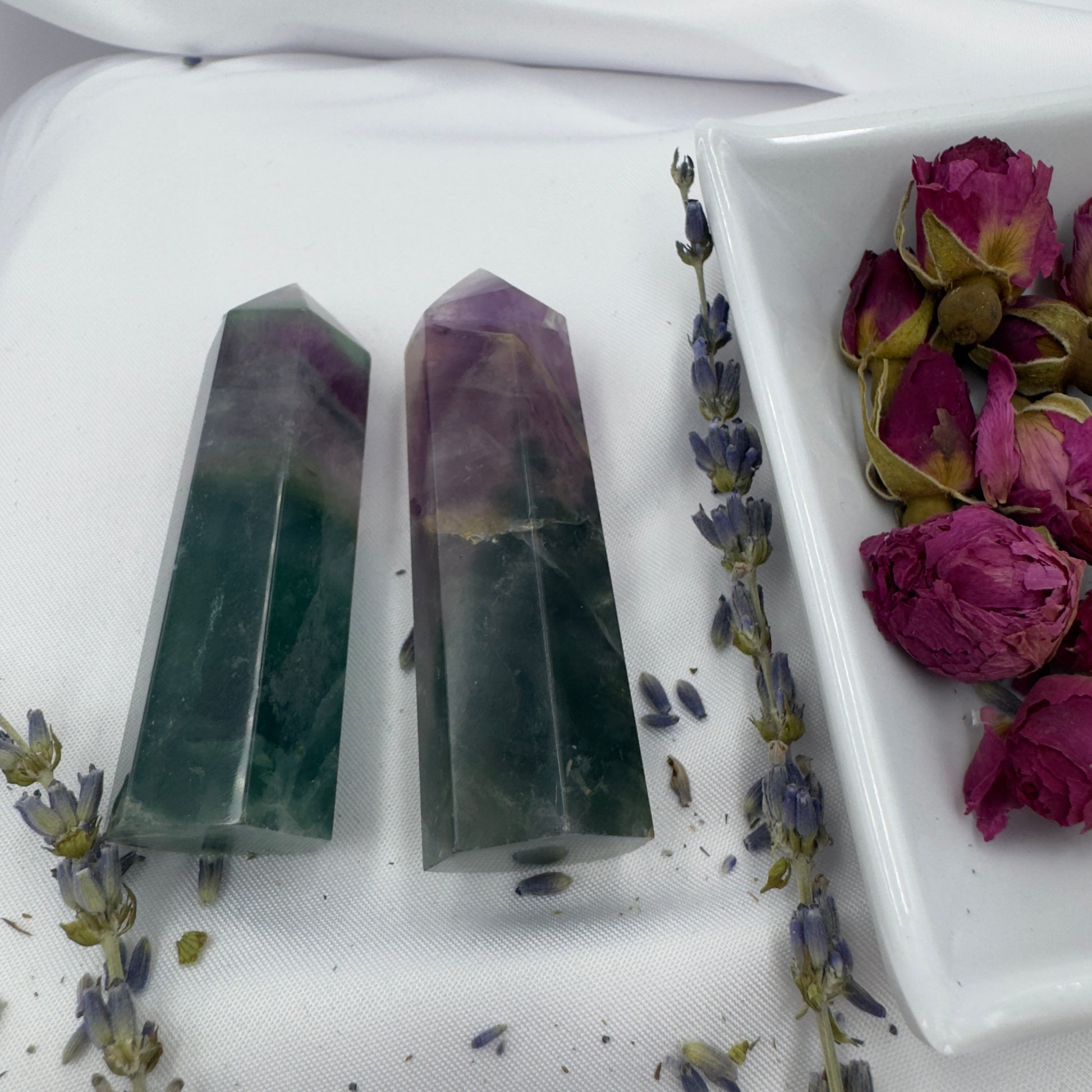 Two polished blue purple green fluorite point crystals displayed on white fabric with dried lavender and roses