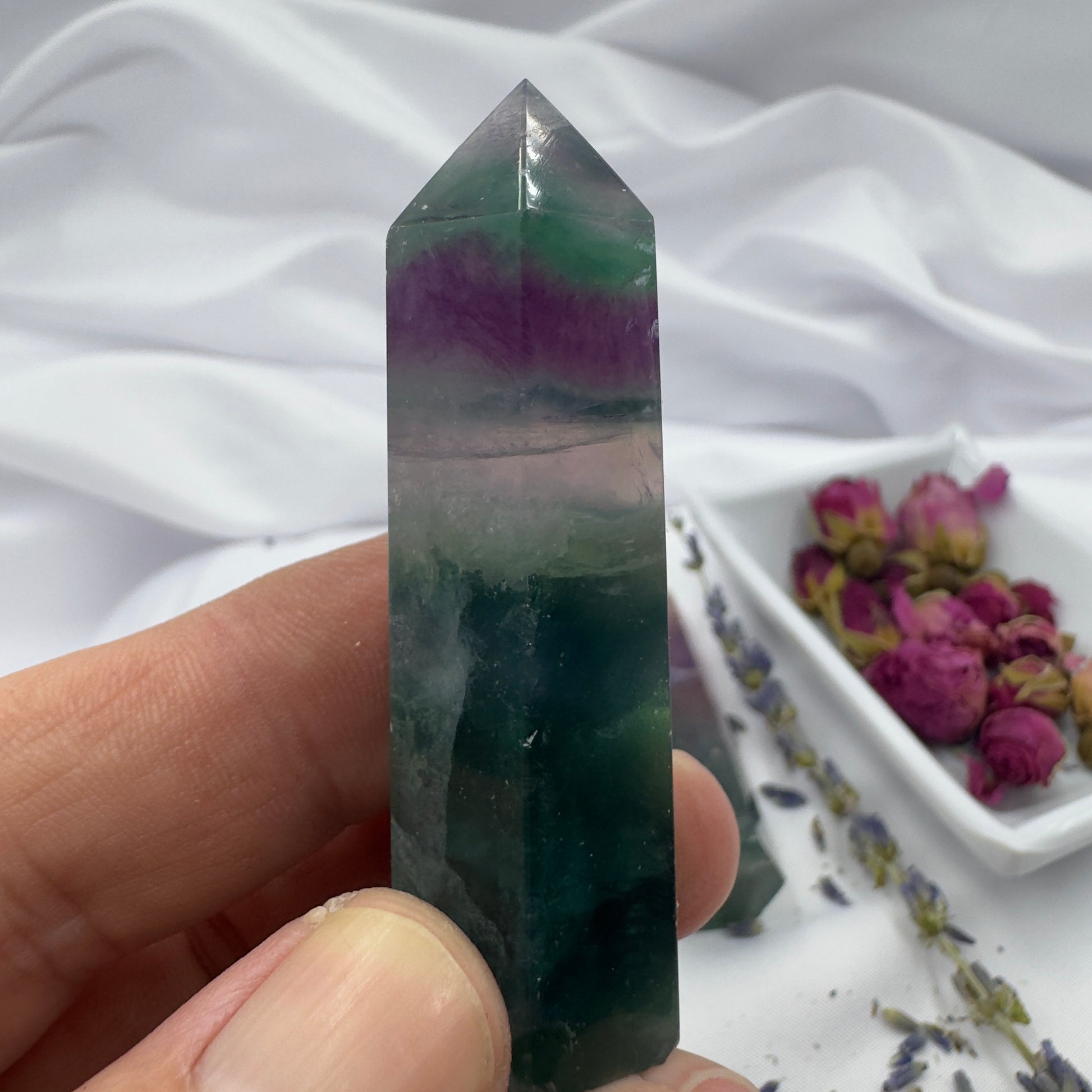 Davinas blue purple green fluorite point held between fingers with dried flowers in background