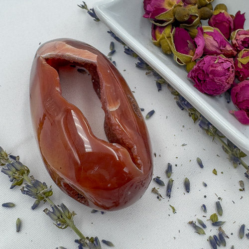 Carnelian Geode Druzy Freeform polished stone displayed with dried lavender and rosebuds on white surface