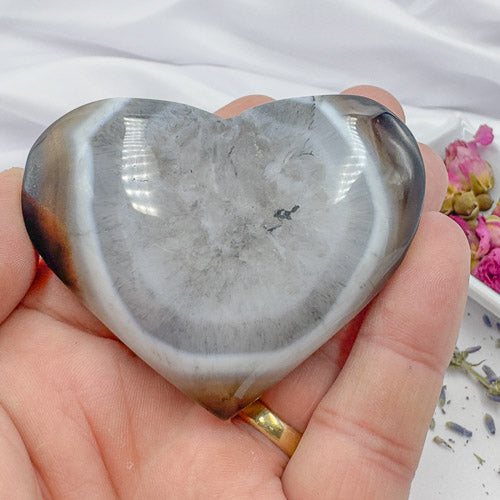 Hand holding a heart-shaped polished crystal stone featuring gray and white patterns premium crystal gifts Davinas