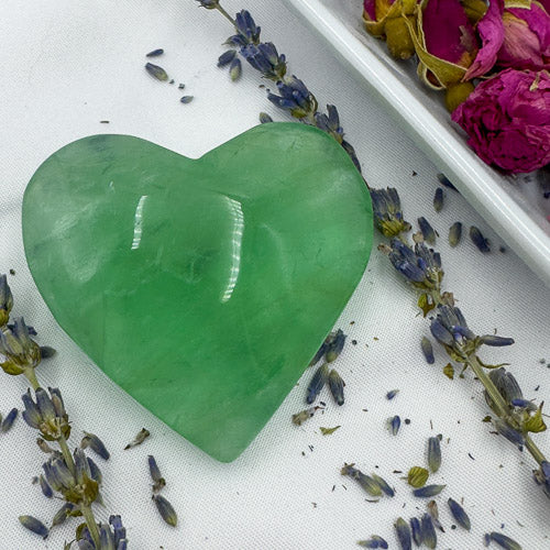 Green heart-shaped fluorite stone surrounded by lavender sprigs and dried roses fluorite love gift