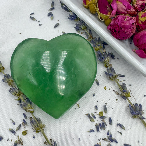 Davinas green fluorite crystal heart surrounded by dried lavender and pink rosebuds on white fabric