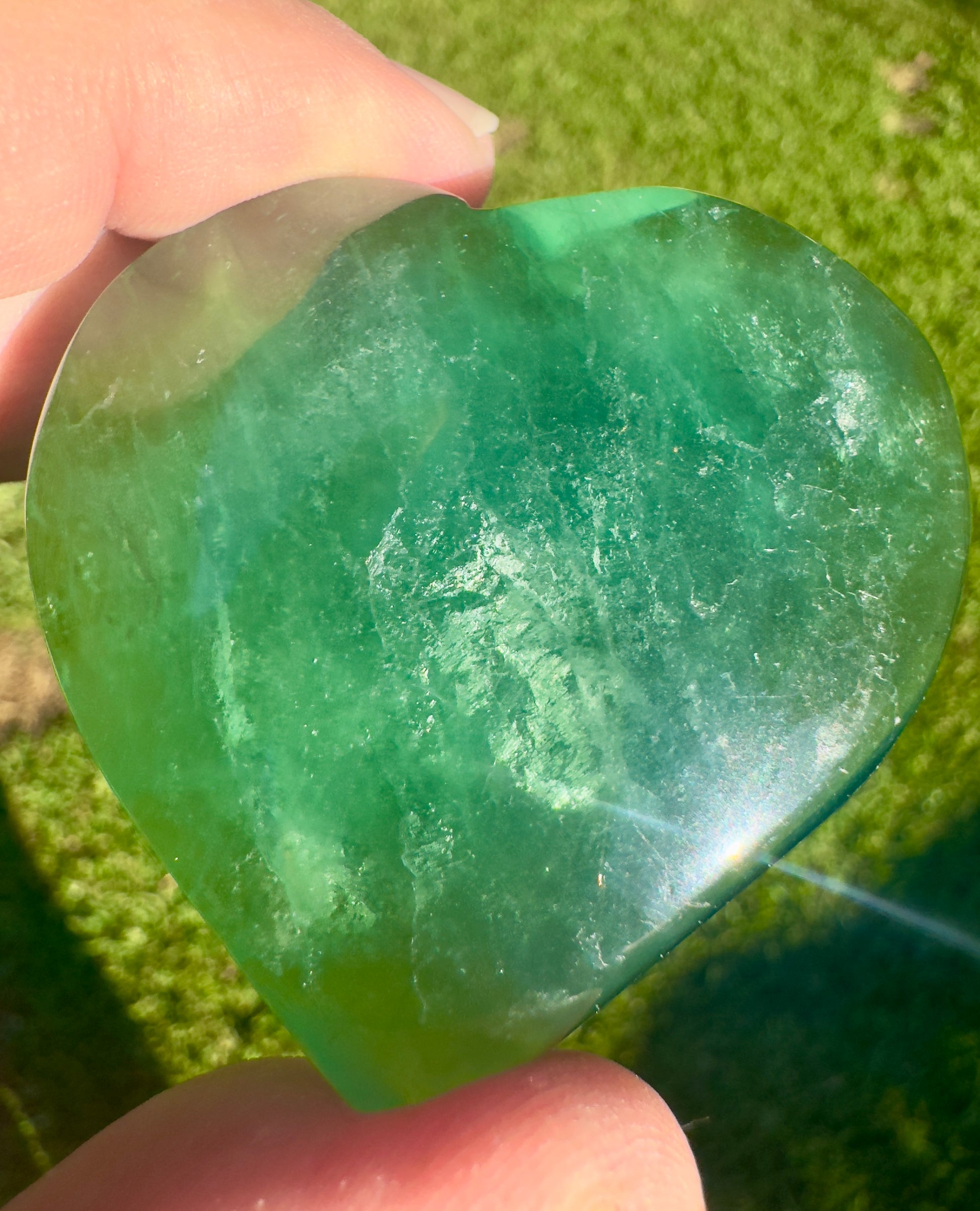 Green fluorite crystal heart held between fingers showcasing its translucent and polished surface