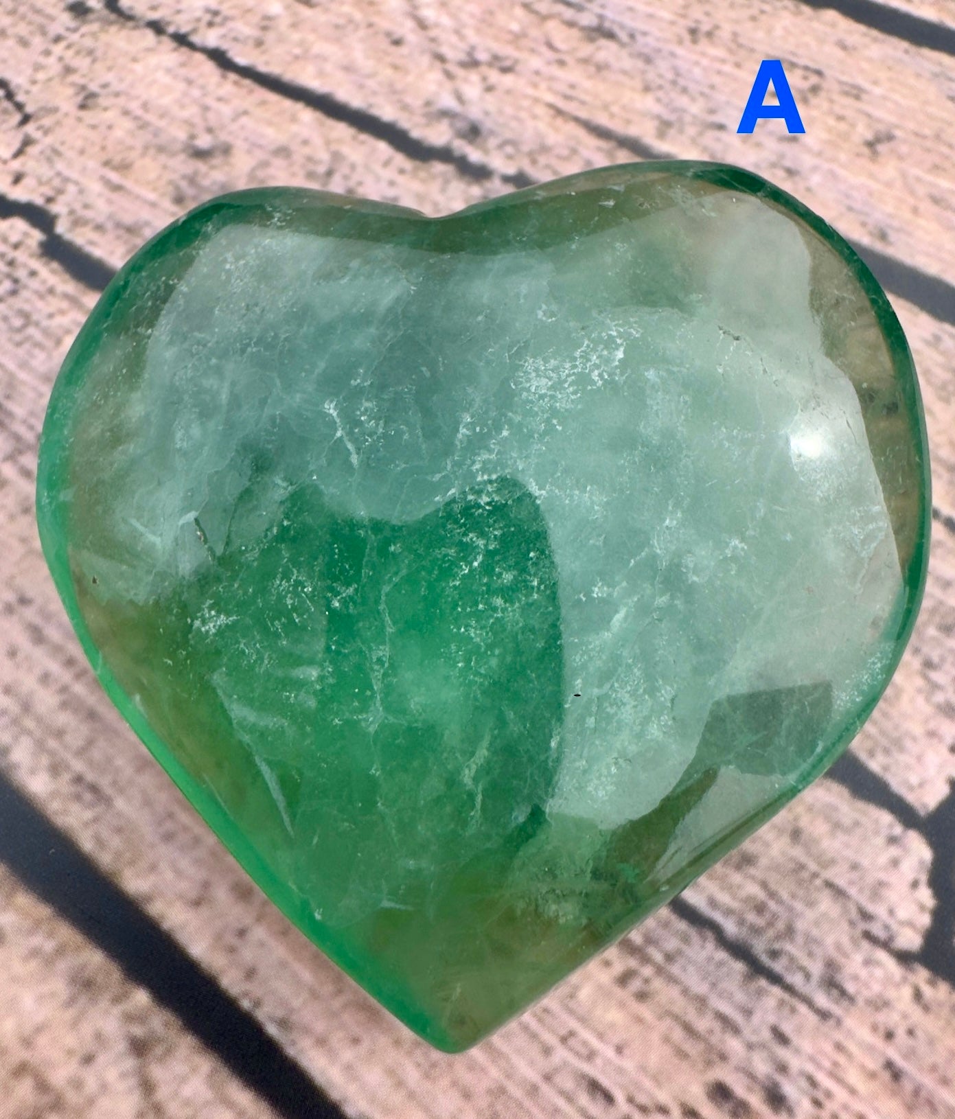 Davinas green fluorite crystal heart with translucent green and white hues on wooden background