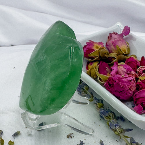 Davinas green fluorite crystal heart displayed on a clear stand with dried roses on a white tray