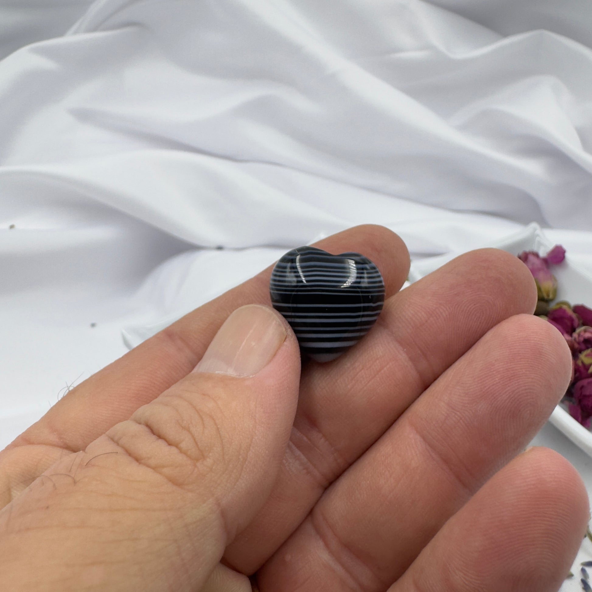 Hand holding a small heart shaped black stripe agate crystal with white stripes on a white background