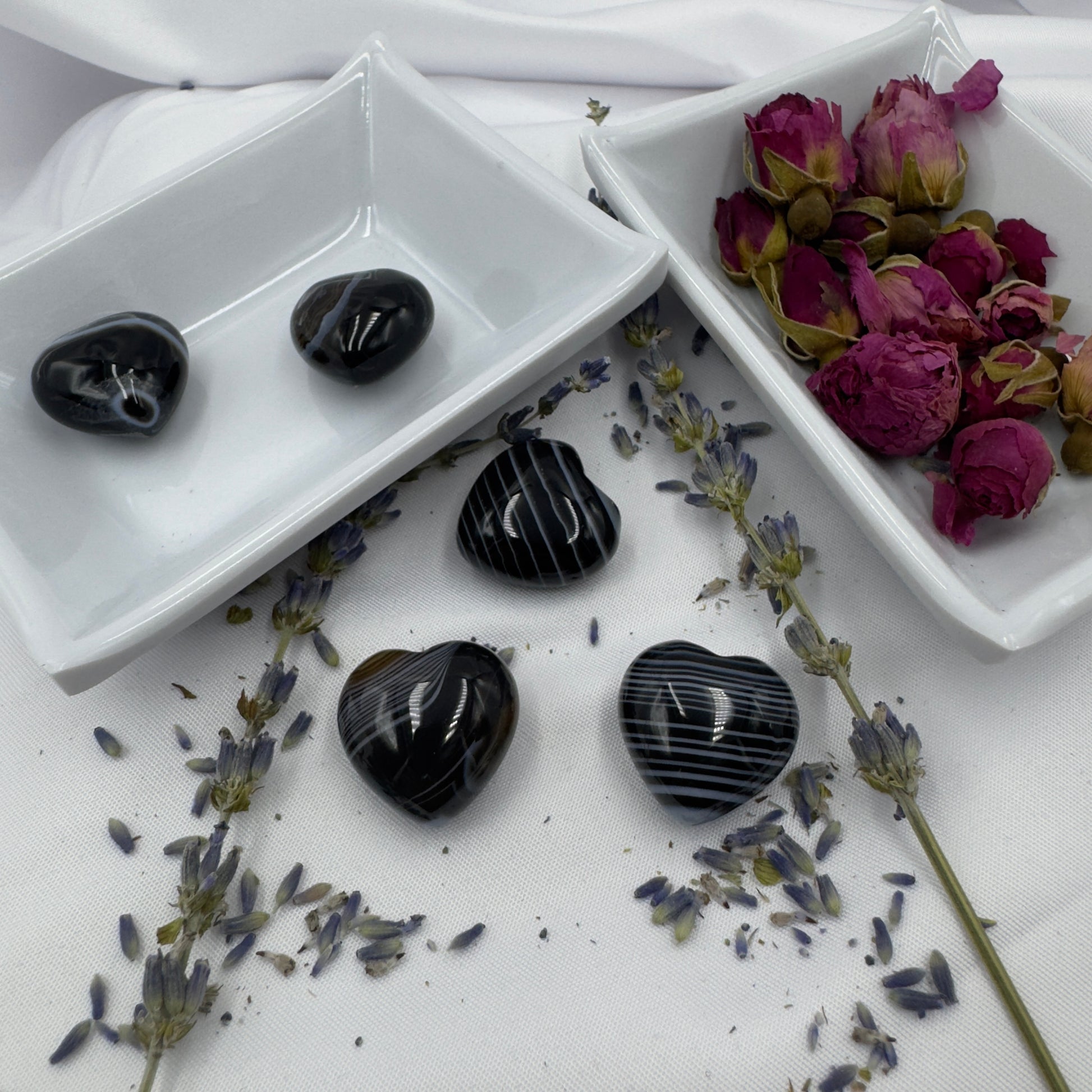 Heart shaped black stripe agate crystal stones displayed with dried flowers on white ceramic trays