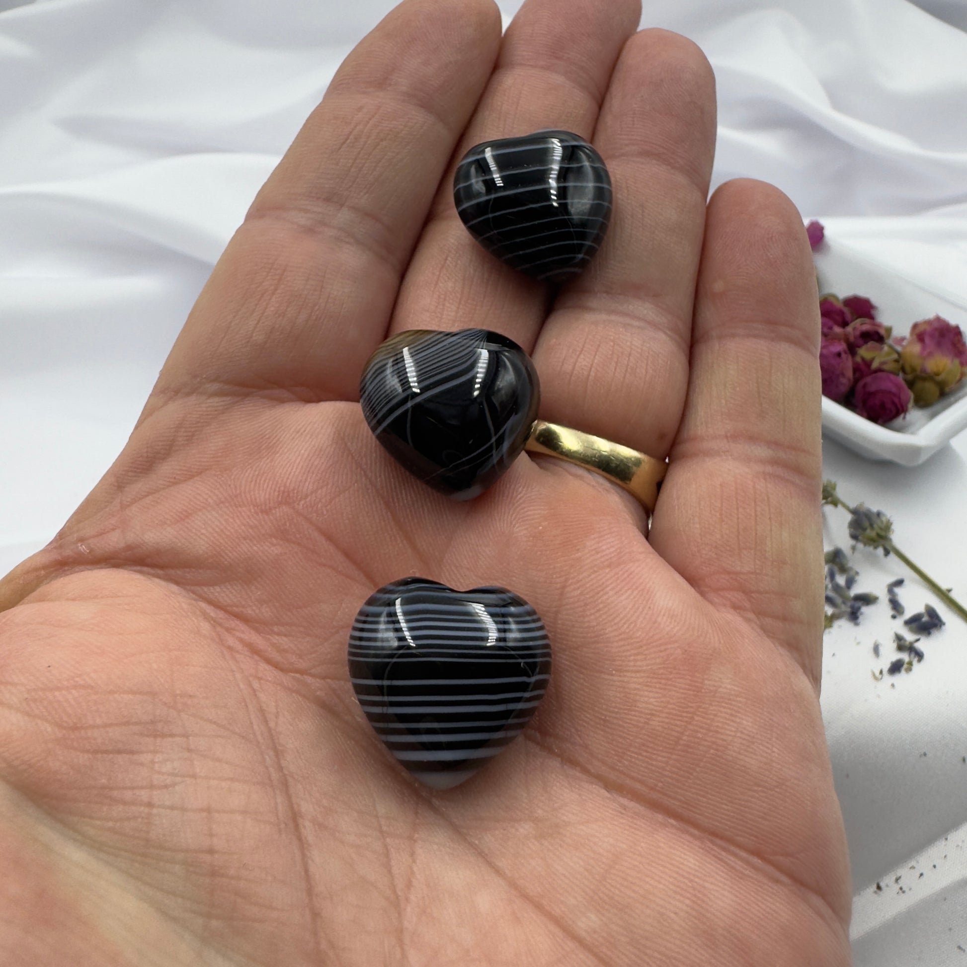 Three heart shaped black stripe agate crystal stones held in a hand with a gold ring