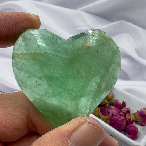 Davinas green heart shaped fluorite crystal held between fingers with dried flowers in background