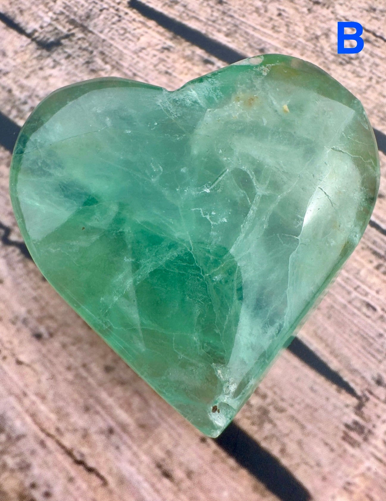 Heart shaped fluorite crystal in green hues by Davinas on wooden background