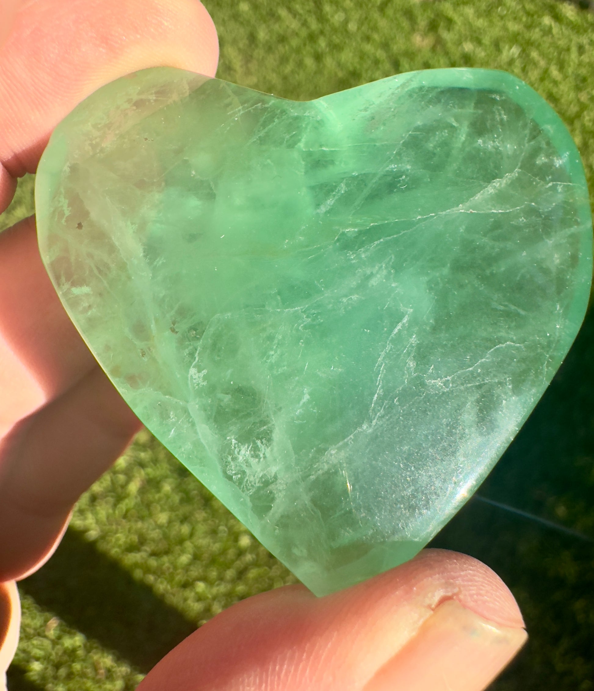 Davinas heart shaped fluorite crystal held between fingers with green and translucent hues