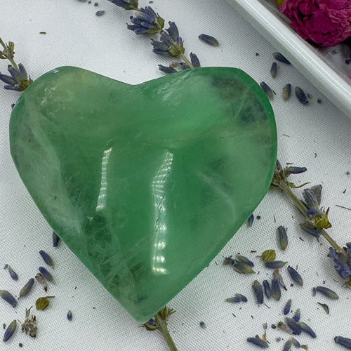Heart shaped fluorite crystal in green placed on a white surface with dried lavender flowers