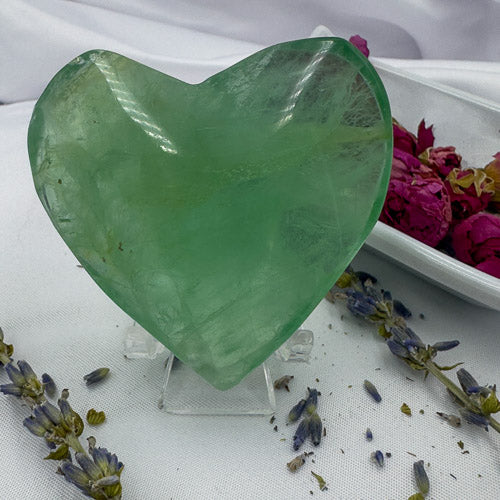 Green heart shaped fluorite crystal displayed on a clear stand with dried flowers around