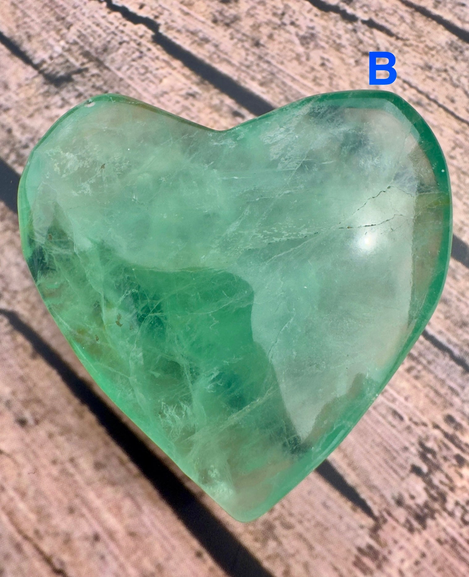 Davinas heart shaped fluorite crystal with green and blue hues on wooden surface