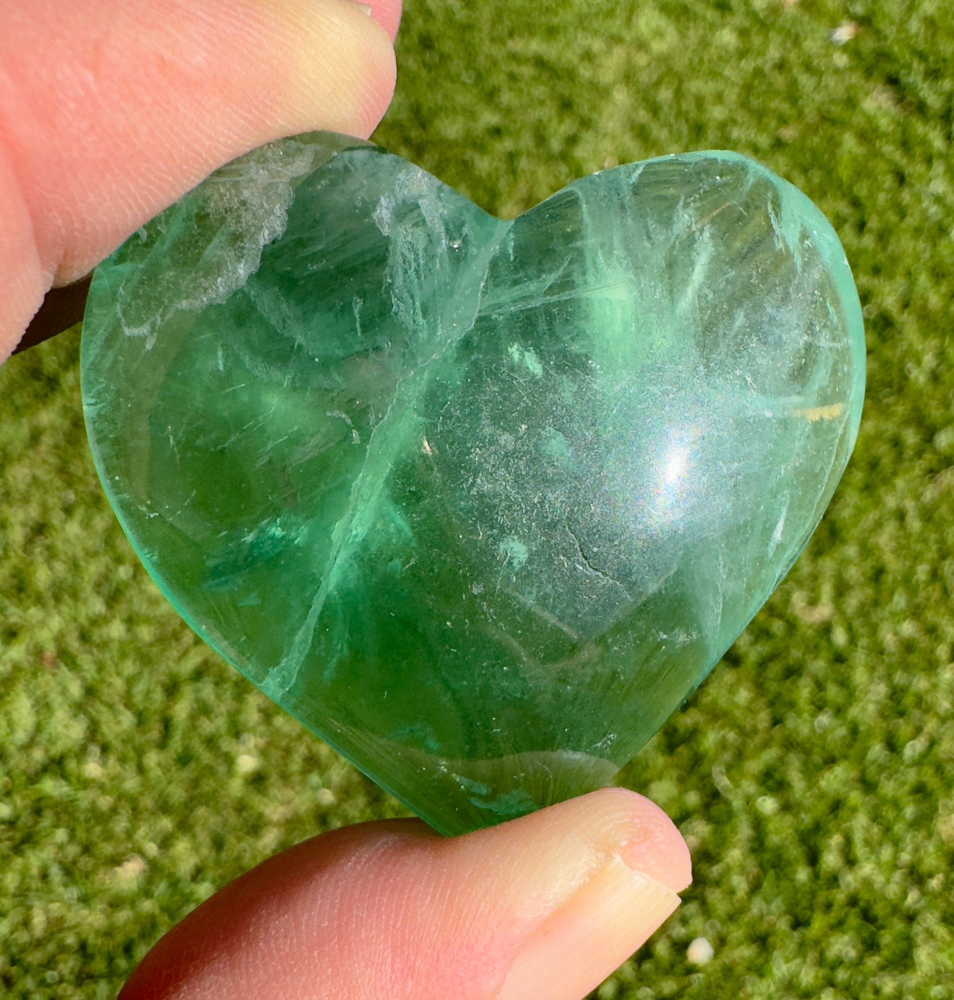 Davinas heart shaped green fluorite held between fingers against a grassy background