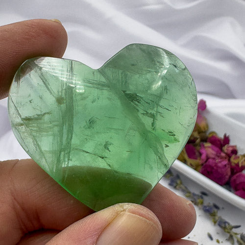 Heart shaped green fluorite crystal held between fingers showcasing its translucent green color and natural patterns