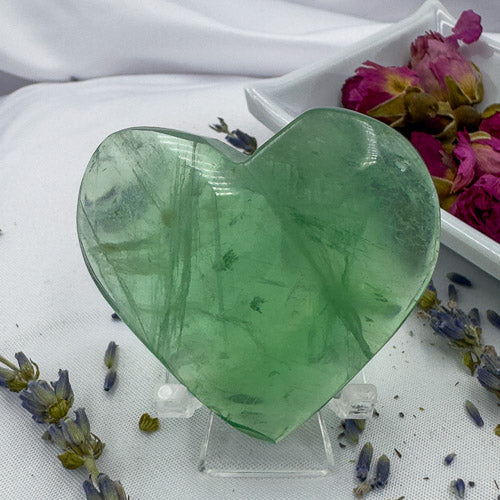 Heart shaped green fluorite crystal displayed on a clear stand with dried flowers around
