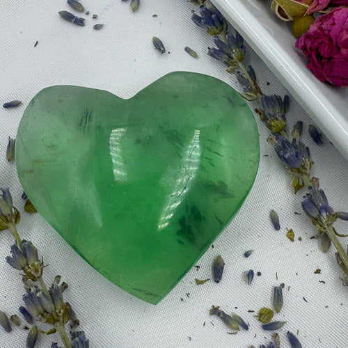 Davinas heart shaped green fluorite stone surrounded by dried lavender flowers on a white surface