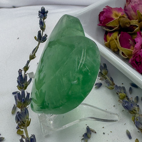 Heart shaped green fluorite crystal displayed with dried lavender and rose petals on white fabric