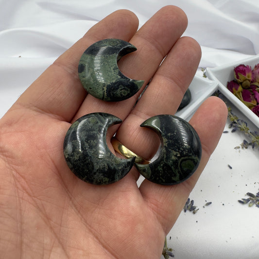 Three crescent-shaped Kambaba Jasper Moon stone crystals held in a hand with a white fabric background