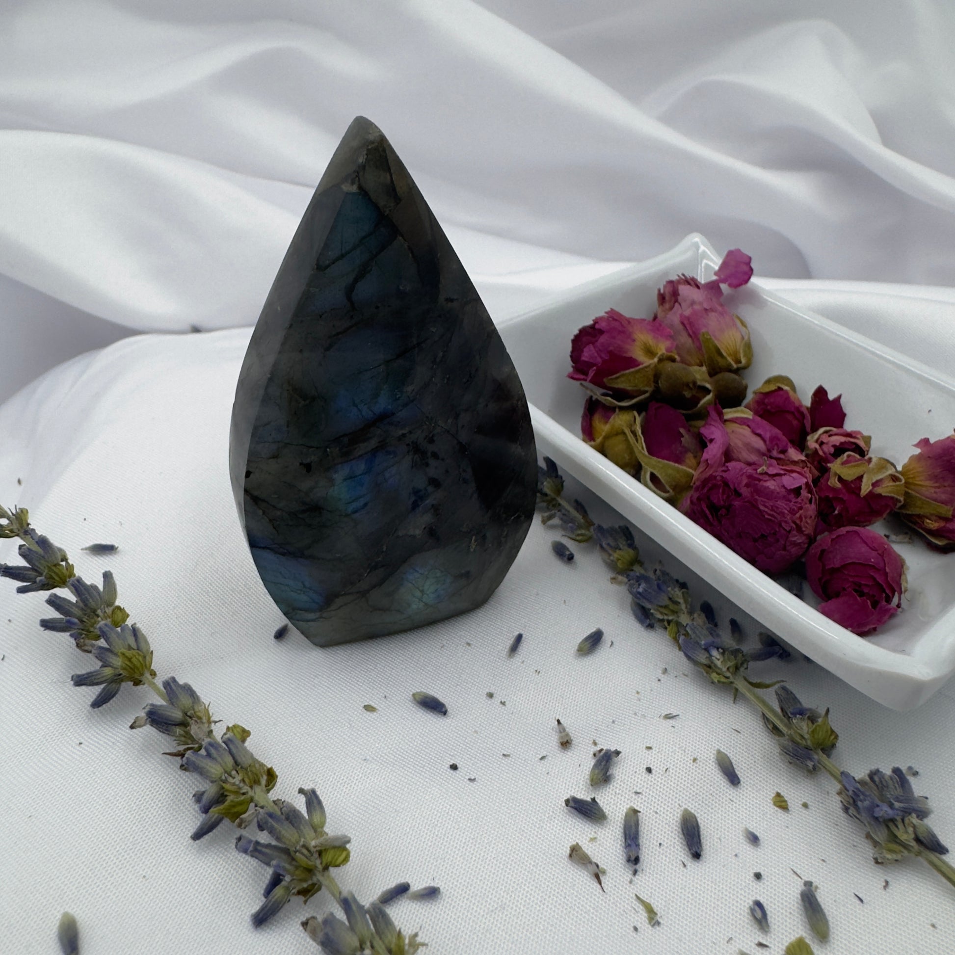 Davinas labradorite freeform crystal with dark iridescent colors displayed on white fabric with dried lavender and rose petals