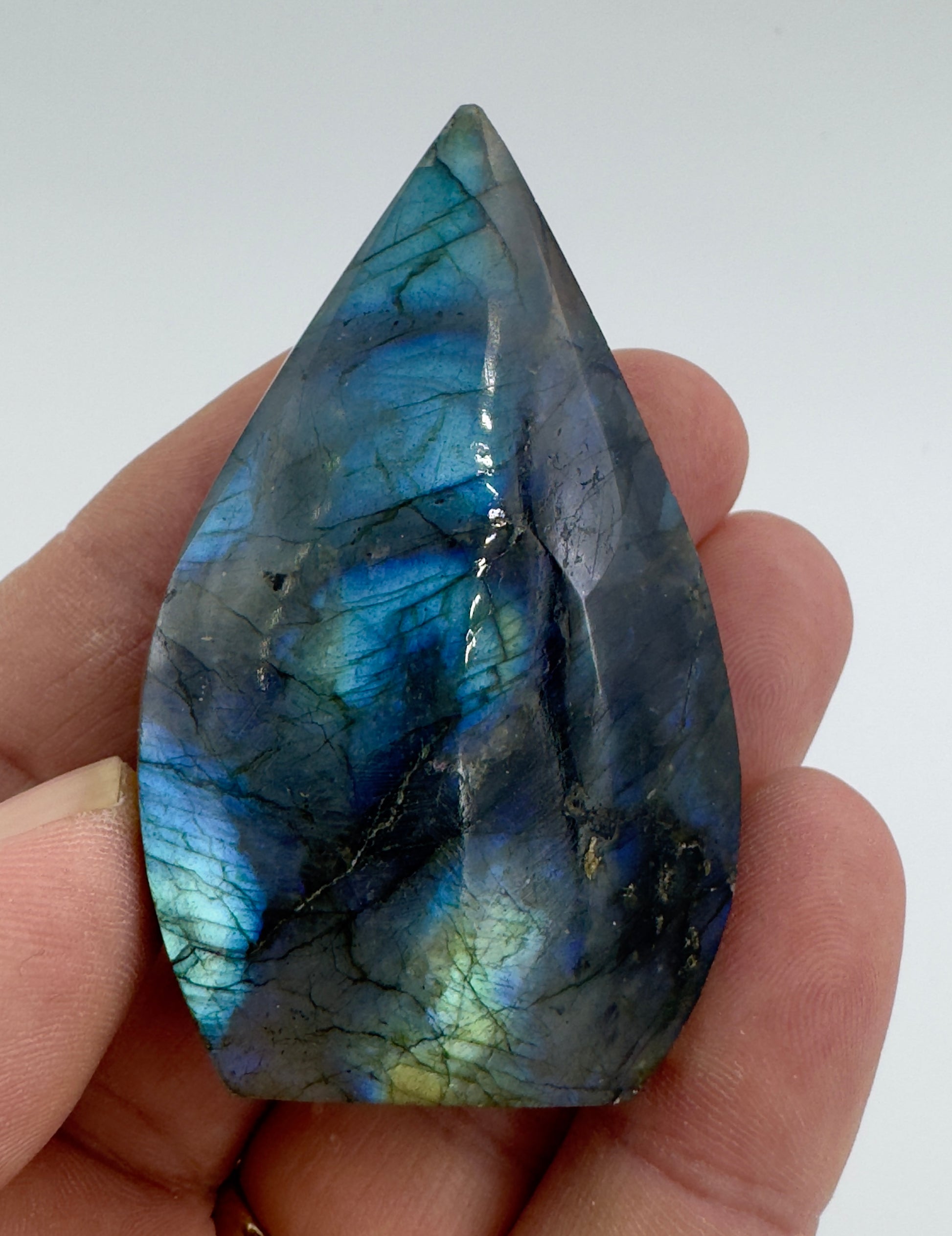 Hand holding a polished Labradorite freeform crystal with vibrant blue and green iridescent colors