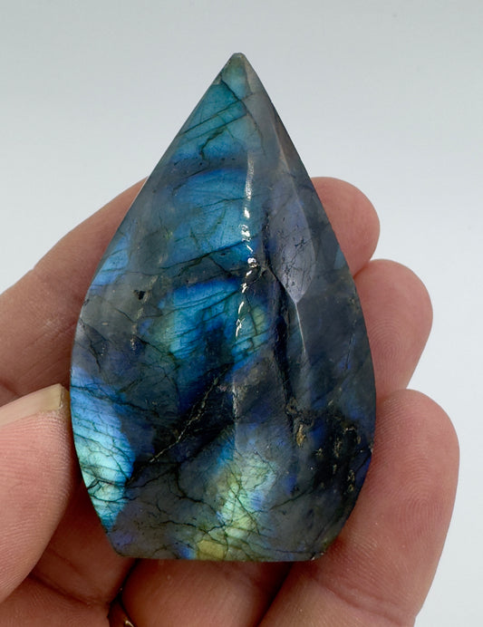Hand holding a polished Labradorite freeform crystal with vibrant blue and green iridescent colors
