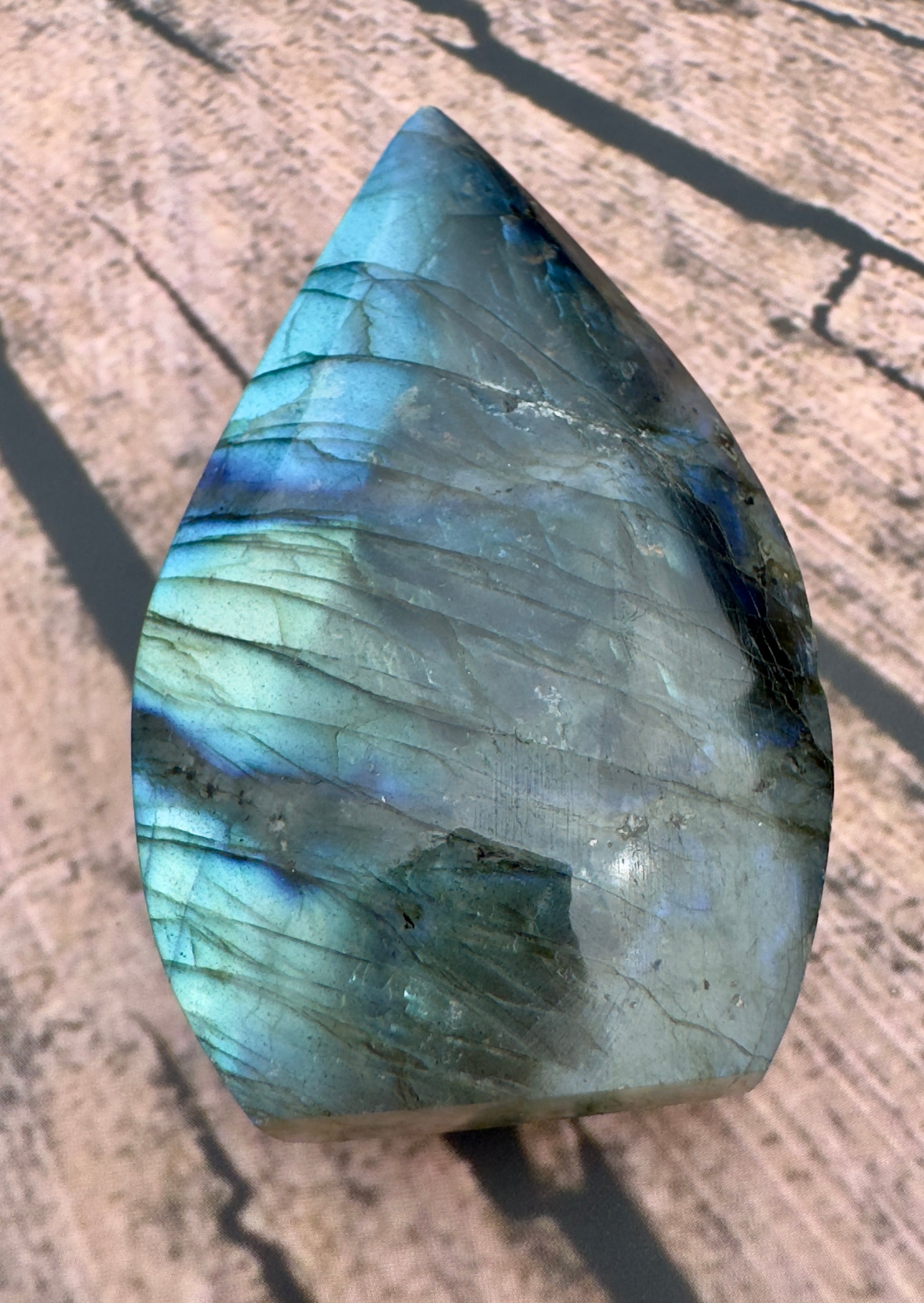 Davinas Labradorite freeform crystal with blue and green iridescent surface on wooden background