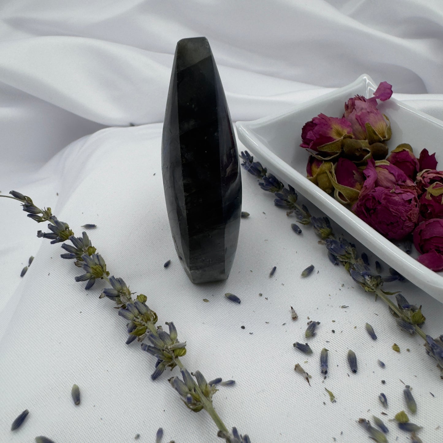Labradorite freeform crystal standing upright on white fabric with dried purple flowers and a white dish